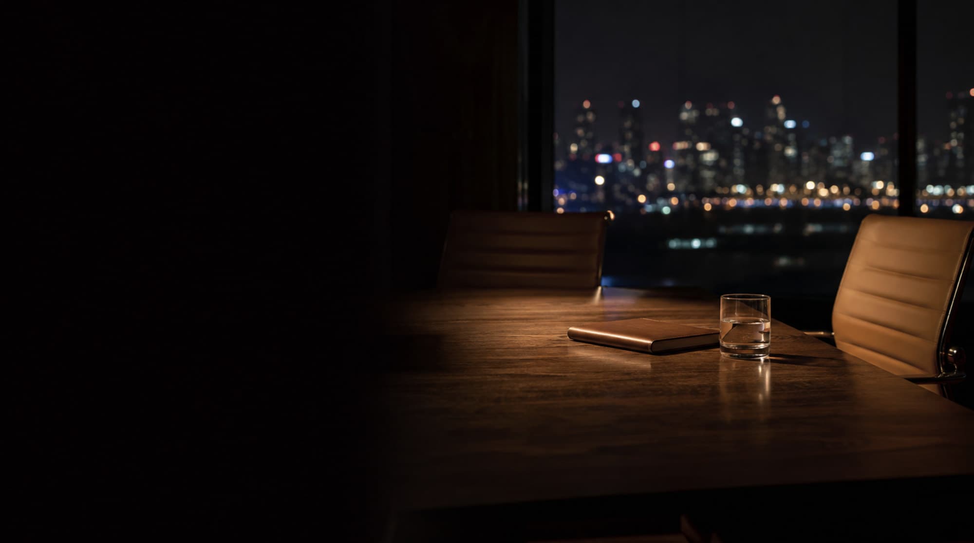 Empty meeting table at night, city lights beyond the glass