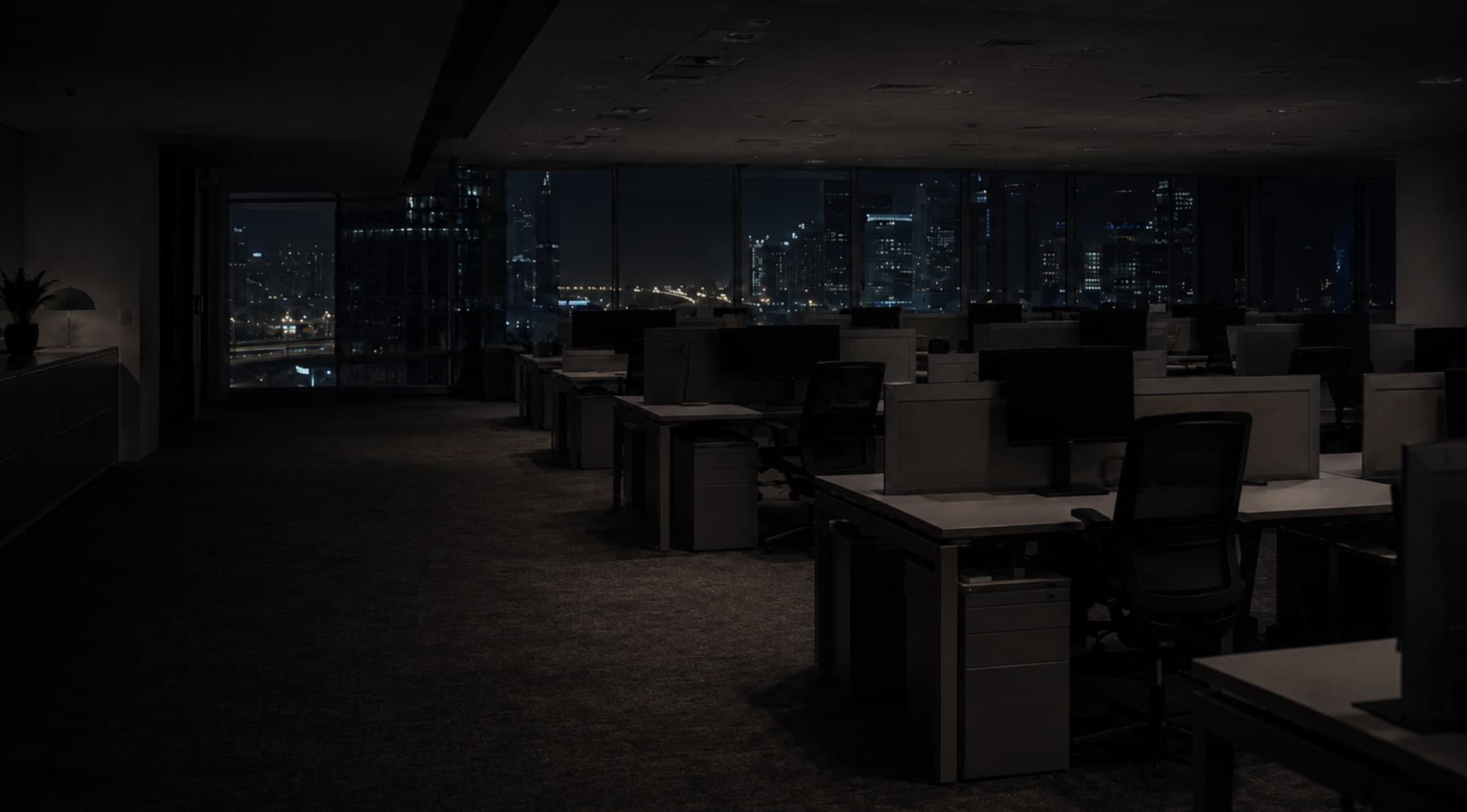 Empty office floor after hours, city lights beyond the glass